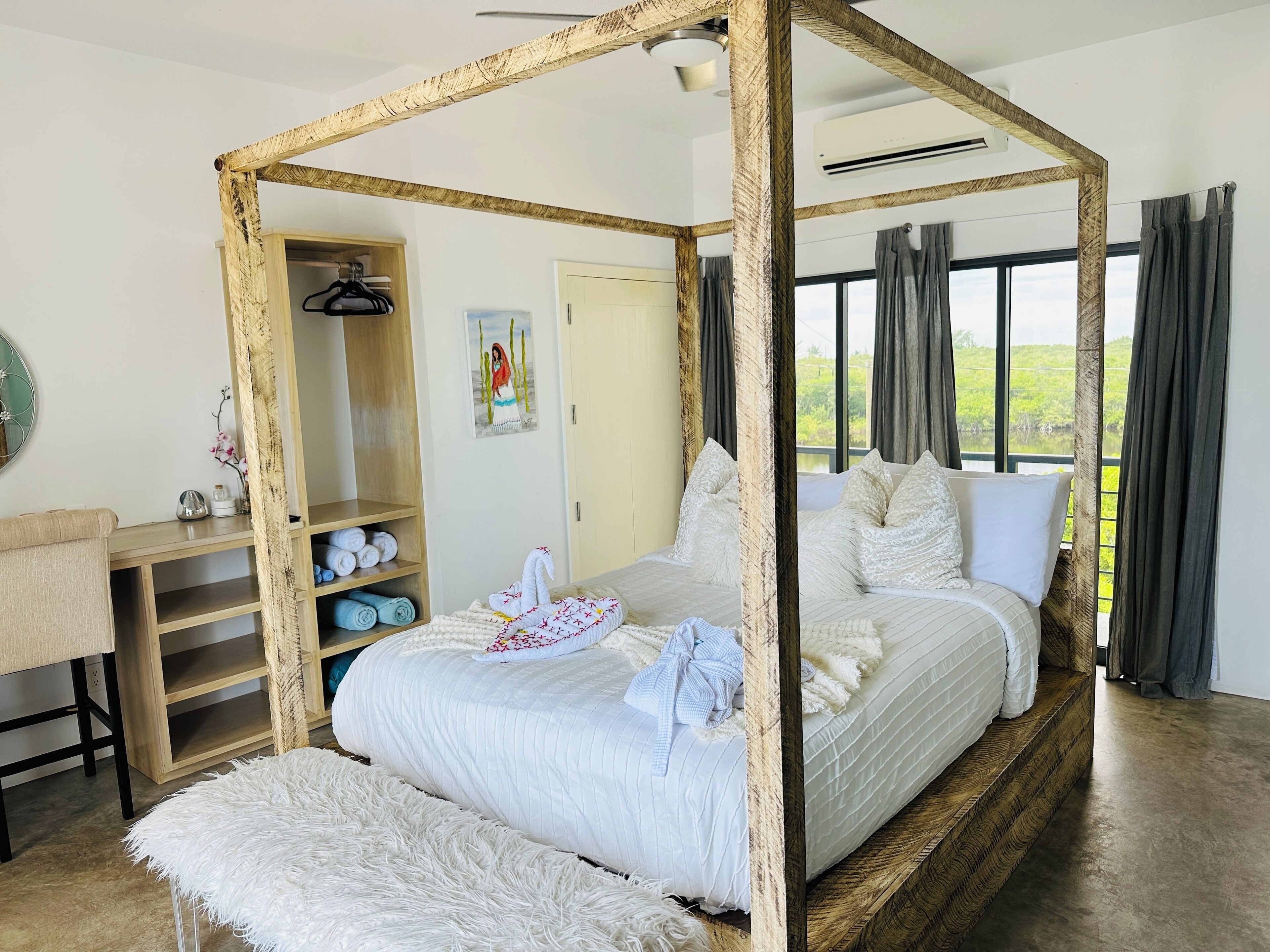 Una cama con dosel con vistas al follaje exterior, un armario de madera y un escritorio con un espejo y un florero.