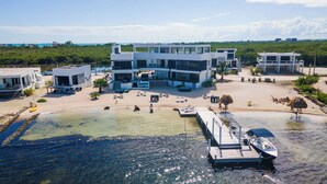 Um resort moderno com vários edifícios, uma área de praia com espreguiçadeiras e um cais com barcos.