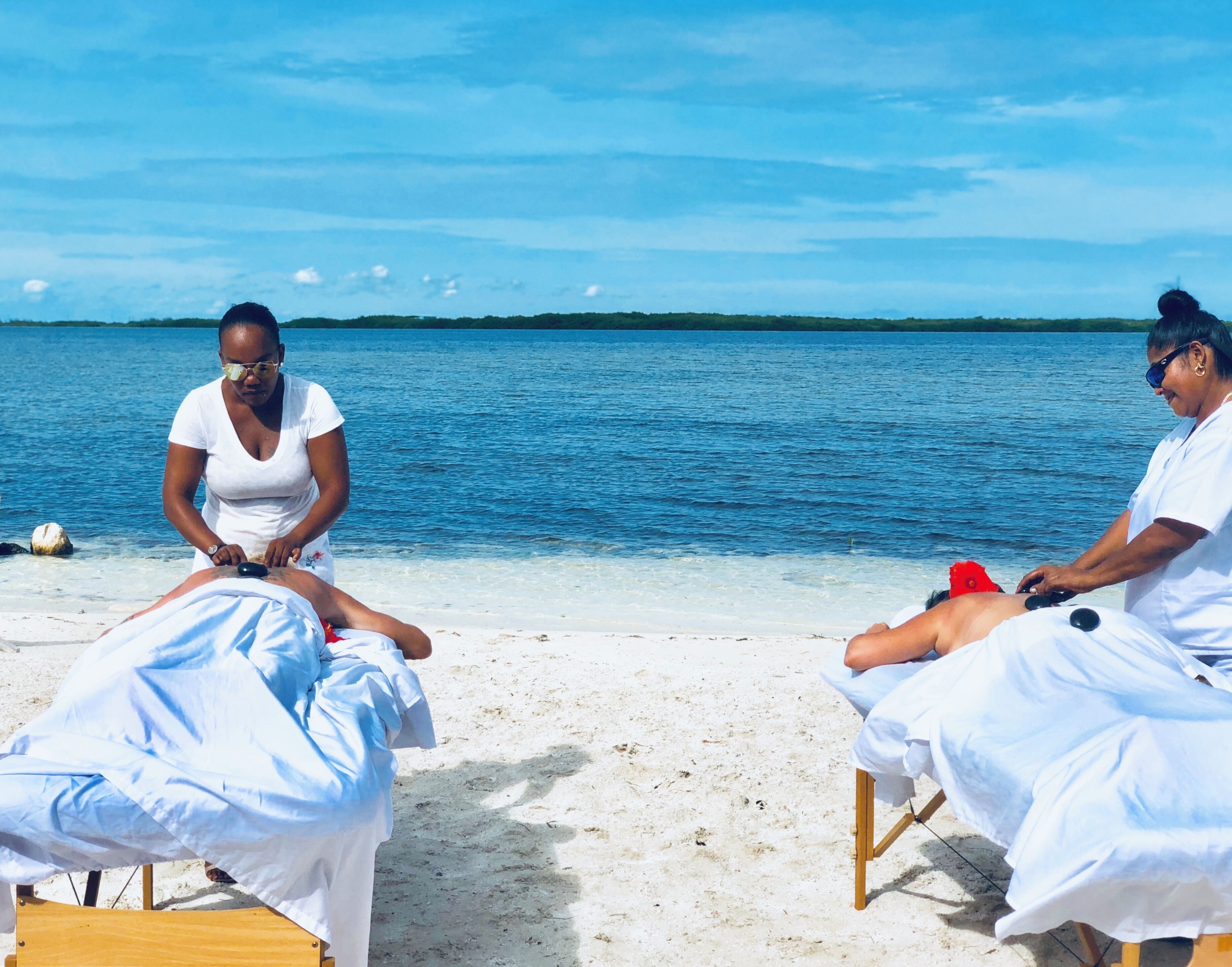 Two massage tables on a beach with a clear view of the ocean and a distant shoreline.