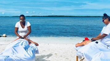 Two massage tables on a beach with a clear view of the ocean and a distant shoreline.