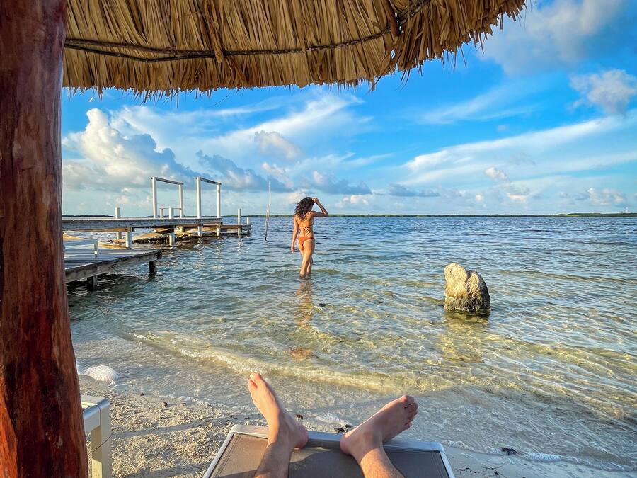 Eine Strandansicht mit einer strohgedeckten Struktur, klarem Wasser und einem weiter entfernten Steg.