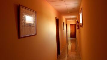 A corridor with orange walls, framed pictures, and a wooden door at the end.