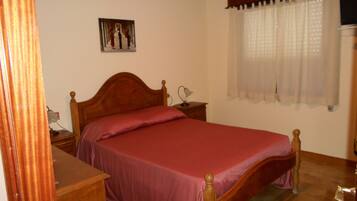 A bedroom with a wooden bed, a nightstand, a lamp, a painting on the wall, and a window with curtains.