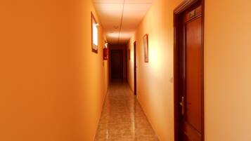 A corridor with orange walls, a wooden door on the right, and a light fixture on the left.