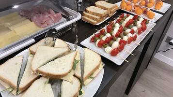 A buffet with various food options including sandwiches, cheese, and fruit skewers.