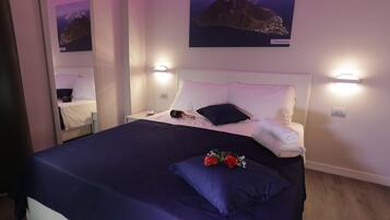 A hotel room with a bed, a nightstand, a lamp, and a wall-mounted mirror.