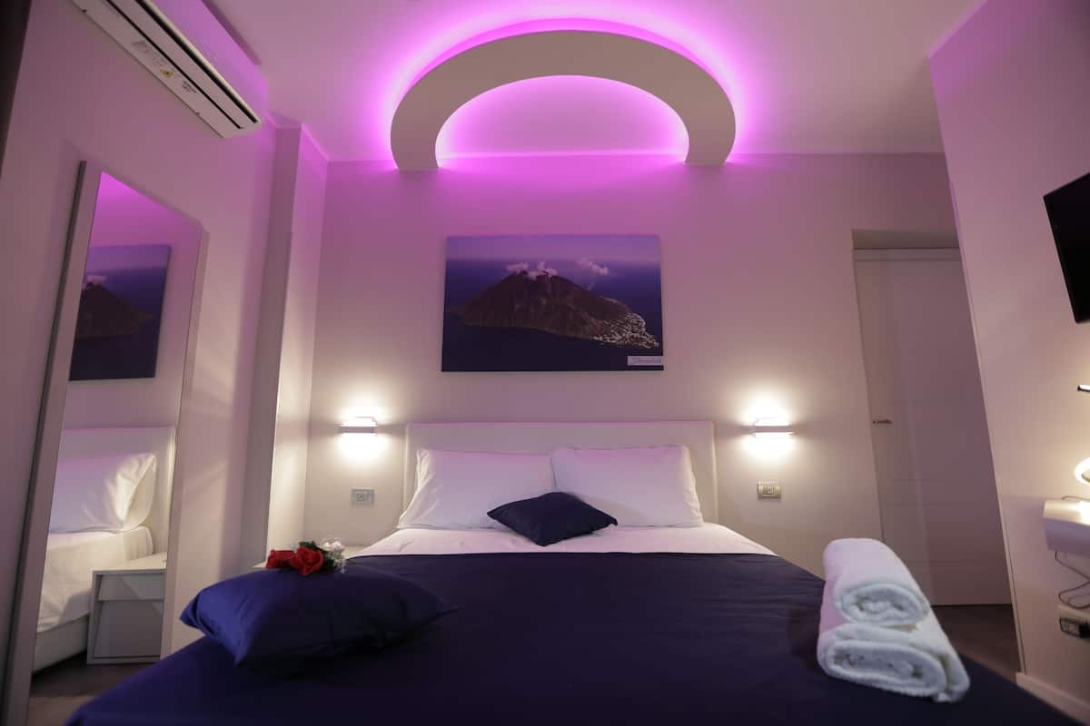 Una camera da letto con un letto, un comodino, uno specchio, una TV a parete e un quadro raffigurante una montagna.