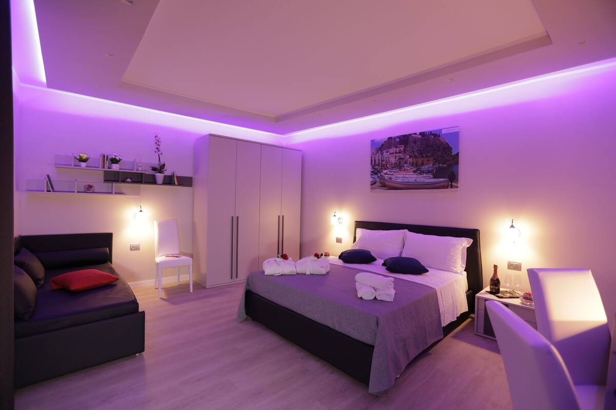 Una camera da letto moderna con un letto, un comodino, una sedia e una mensola a parete con libri e piante.