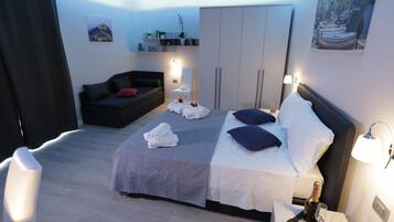 Quarto de hotel moderno com uma cama, um sofá, um guarda-roupa e uma mesinha com uma garrafa e copos.