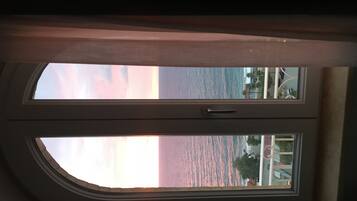 A view through a window with a view of the ocean and a building with palm trees.