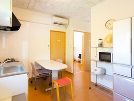 Una cocina compacta con estufa a gas, un lavamanos, una mesa de comedor blanca con sillas, un taburete pequeño y un microondas sobre una repisa metálica.