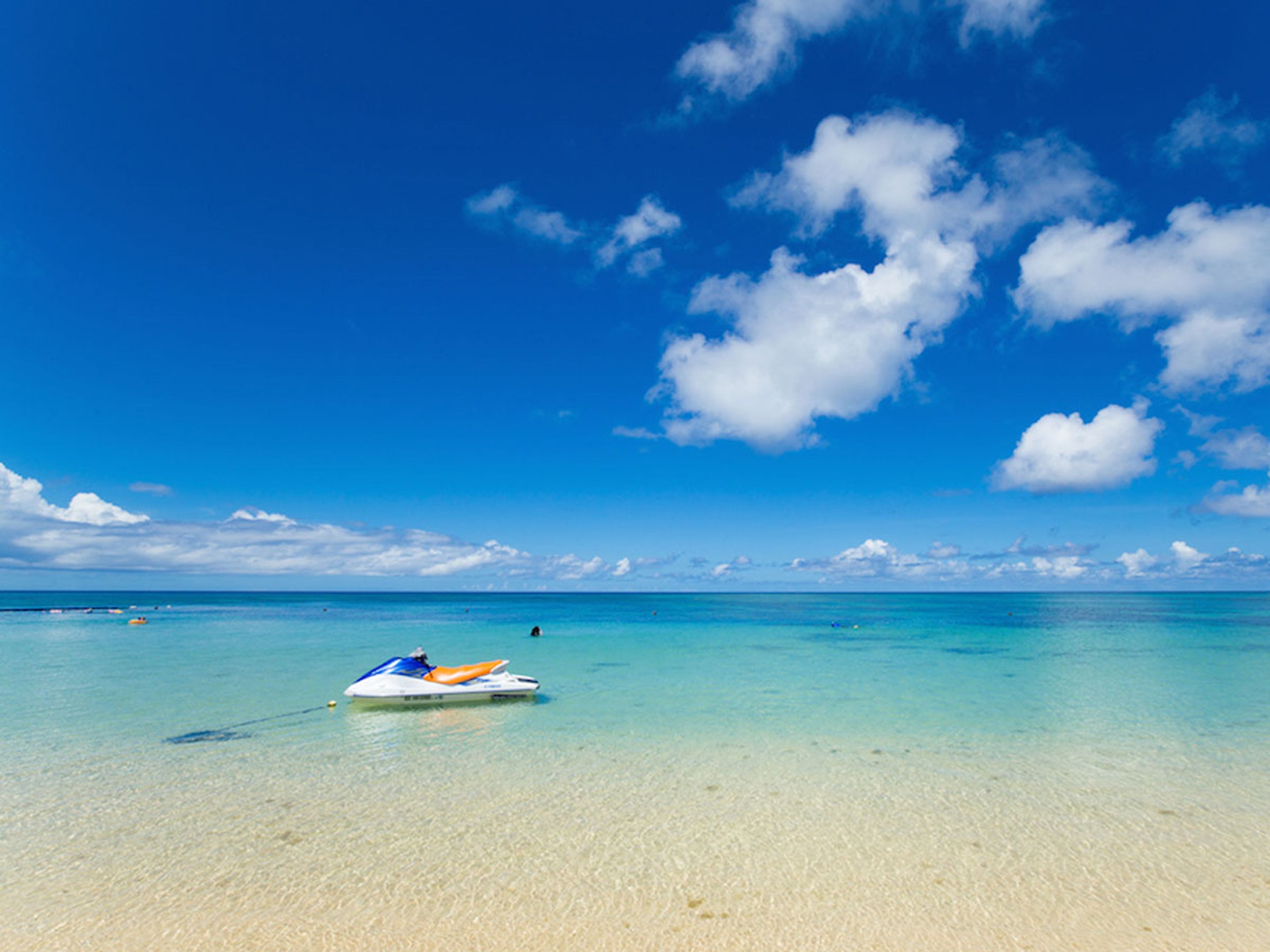 A clear blue sky, a sandy beach, and a jet ski in the water.