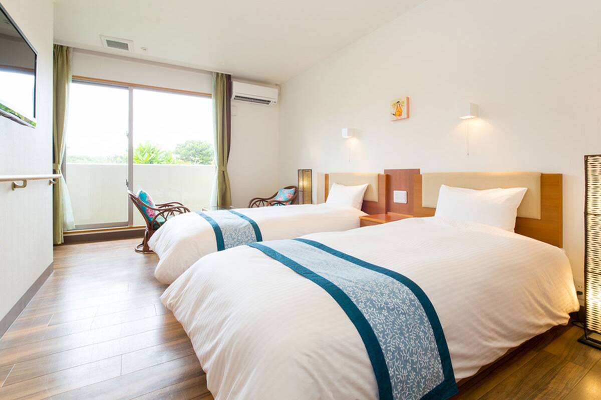 Habitació d'hotel amb dos llits, un balcó amb una cadira i vistes a la vegetació exterior.