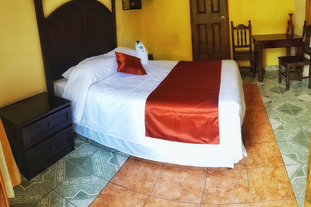 A bed with white and red bedding, a nightstand, a wooden door, a chair, and a small table.