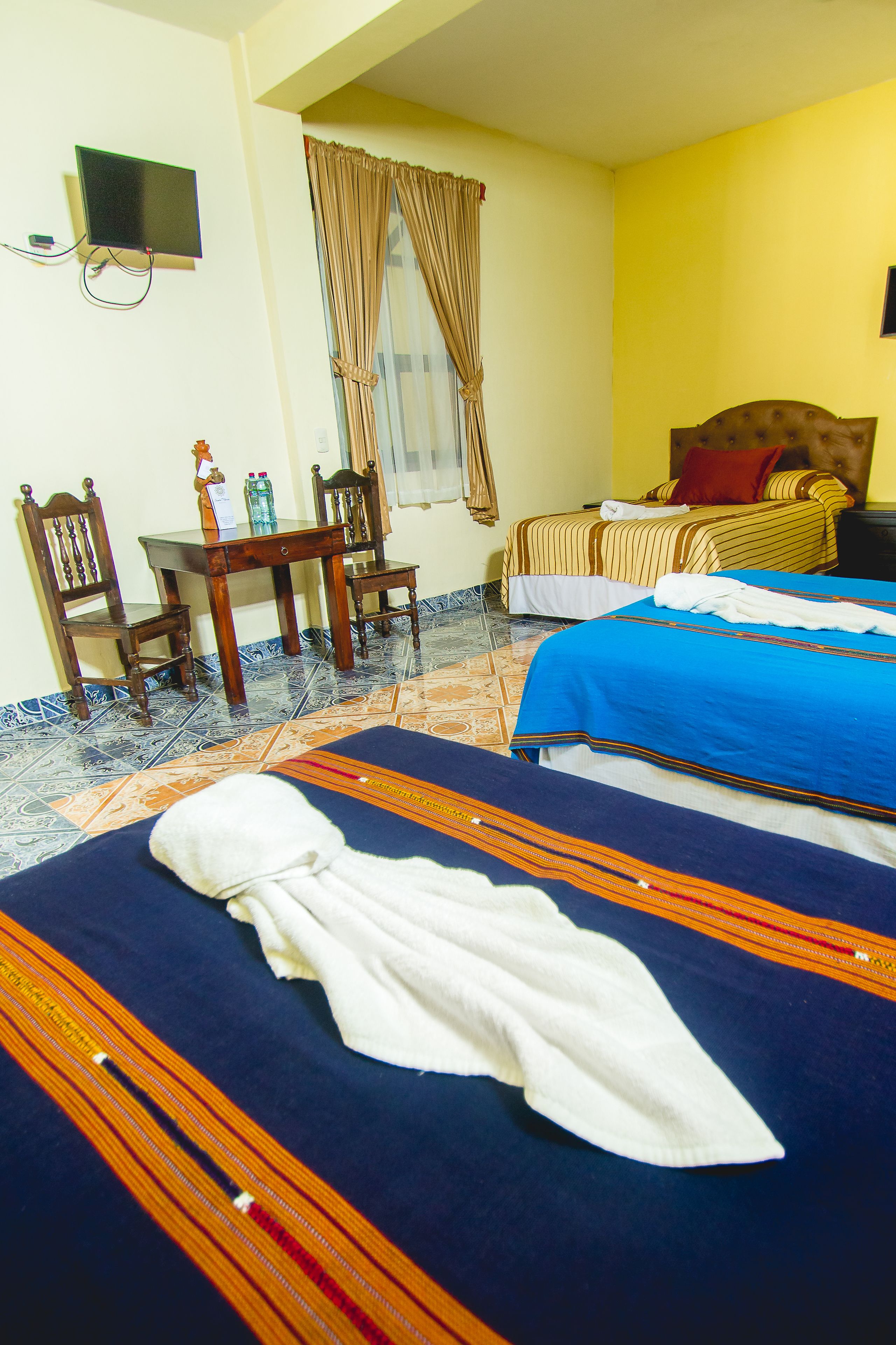 A hotel room with two beds, a desk with chairs, a television, and a window with curtains.