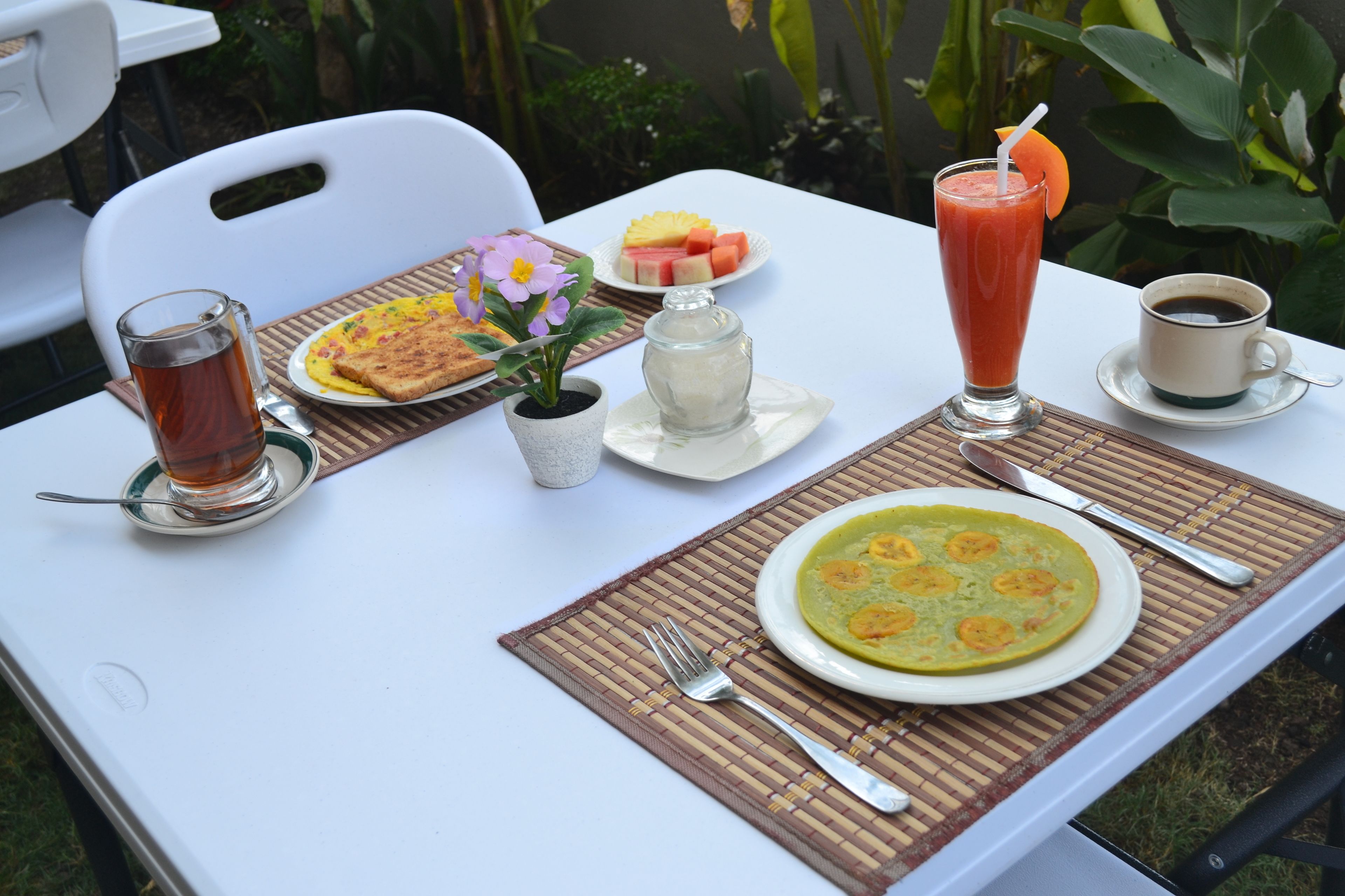A table set with a plate of food, a glass of tea, a cup of coffee, and a fruit plate.