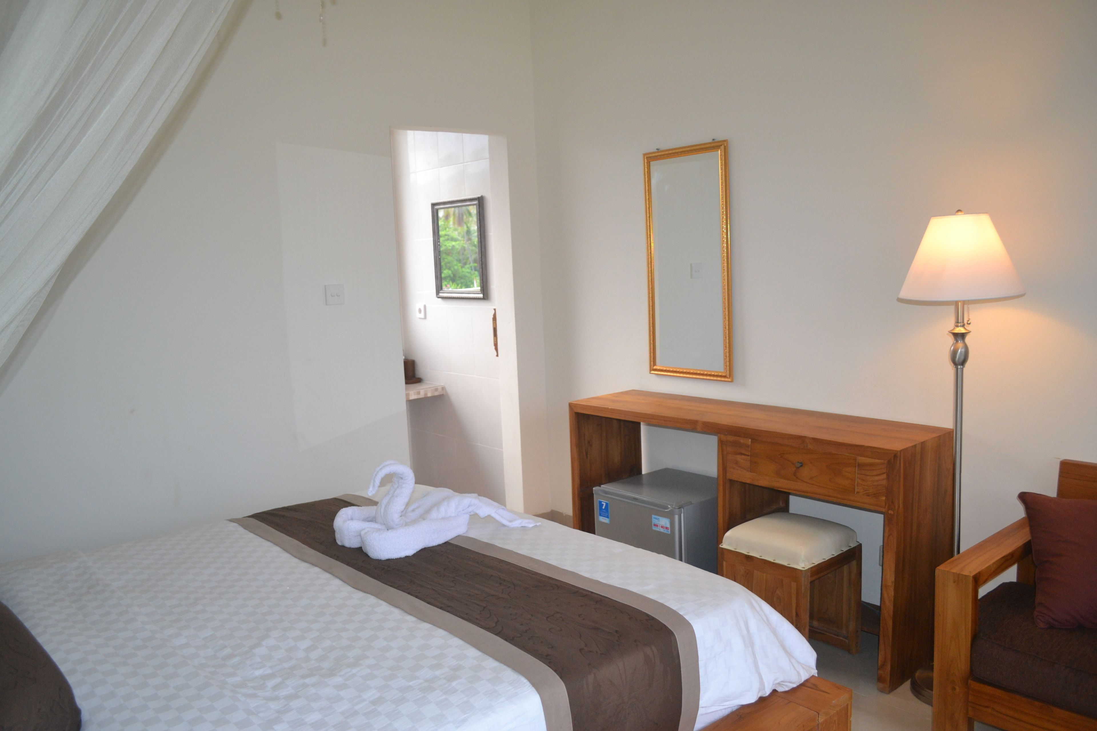 A hotel room with a bed, a desk, a chair, a lamp, and a refrigerator.