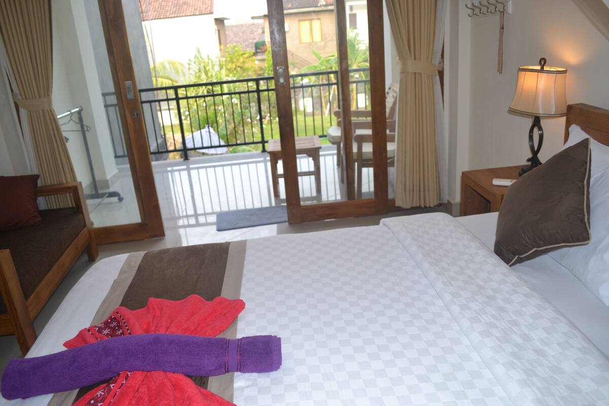 A hotel room with a bed, a nightstand, a lamp, a chair, and a view of the outside balcony.