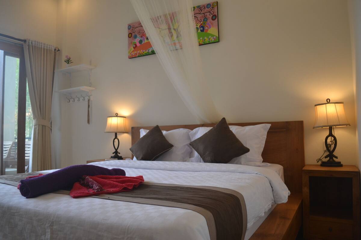 A neatly made bed with a wooden headboard, two bedside lamps, and a window with curtains.