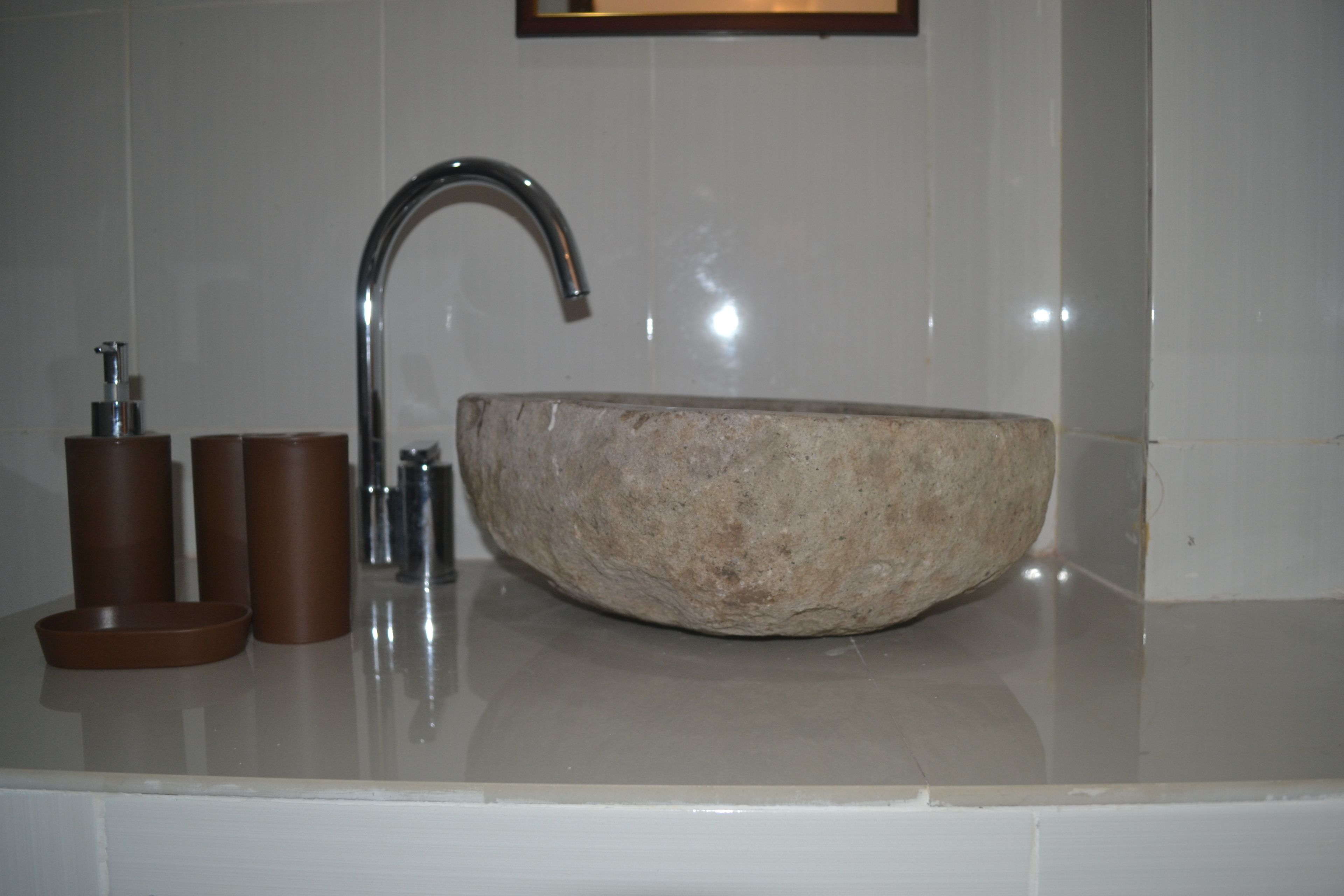 Une salle de bain avec un grand lavabo en pierre de forme ronde, un robinet moderne et un miroir au-dessus du lavabo.