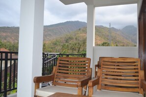 A balcony with two wooden chairs and a table, overlooking a mountainous landscape. - Master Homestay (Karangasem)