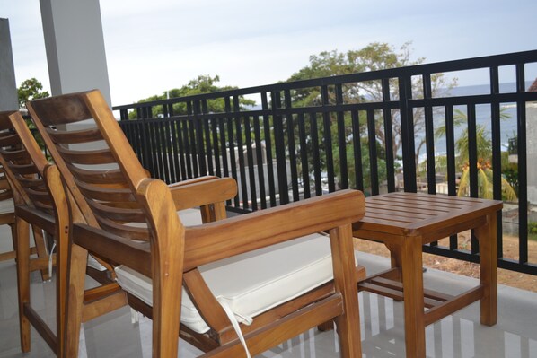 A wooden outdoor seating area with a table and two chairs, overlooking a scenic view of the sea and greenery.