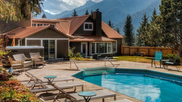 Area piscina con poltrone relax e vasca idromassaggio, circondata da un solarium in legno con vista sulle montagne.