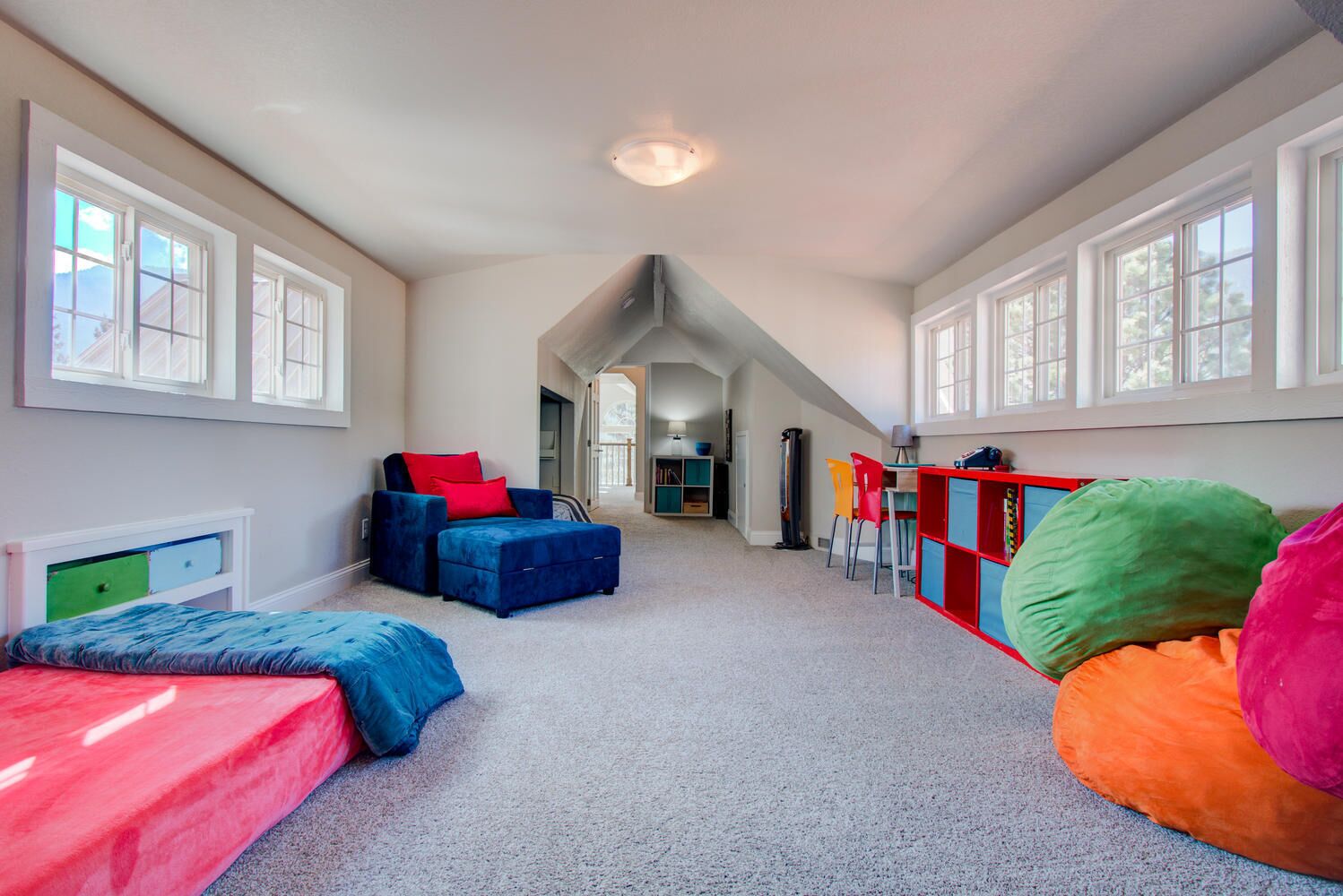 A spacious room with a high ceiling, large windows, and a cozy seating area with colorful cushions.