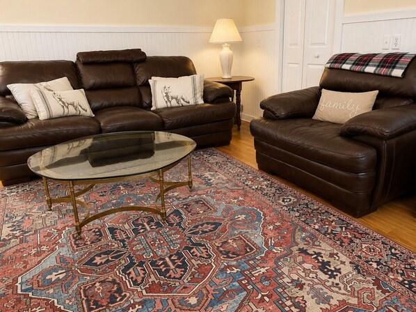 A living room with a brown leather sofa, a glass coffee table, and a patterned rug.