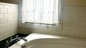 A bathroom with a white bathtub, a window with floral curtains, and white tiled walls.