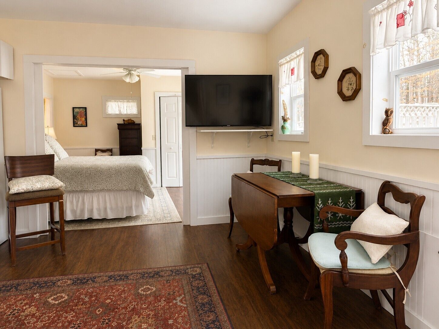A bedroom with a bed, a desk, a chair, a television, and a window with curtains.