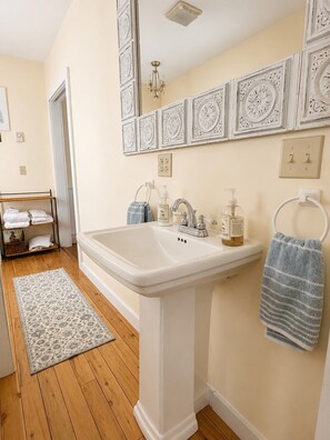 A bathroom with a white pedestal sink, a towel rack, and a patterned rug on the floor. - Lake Placid Village Cottage in Fall! (Lake Placid)