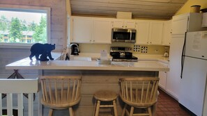 A kitchen with white cabinets, a stainless steel oven, a microwave, and a refrigerator. There are two wooden chairs at the counter.