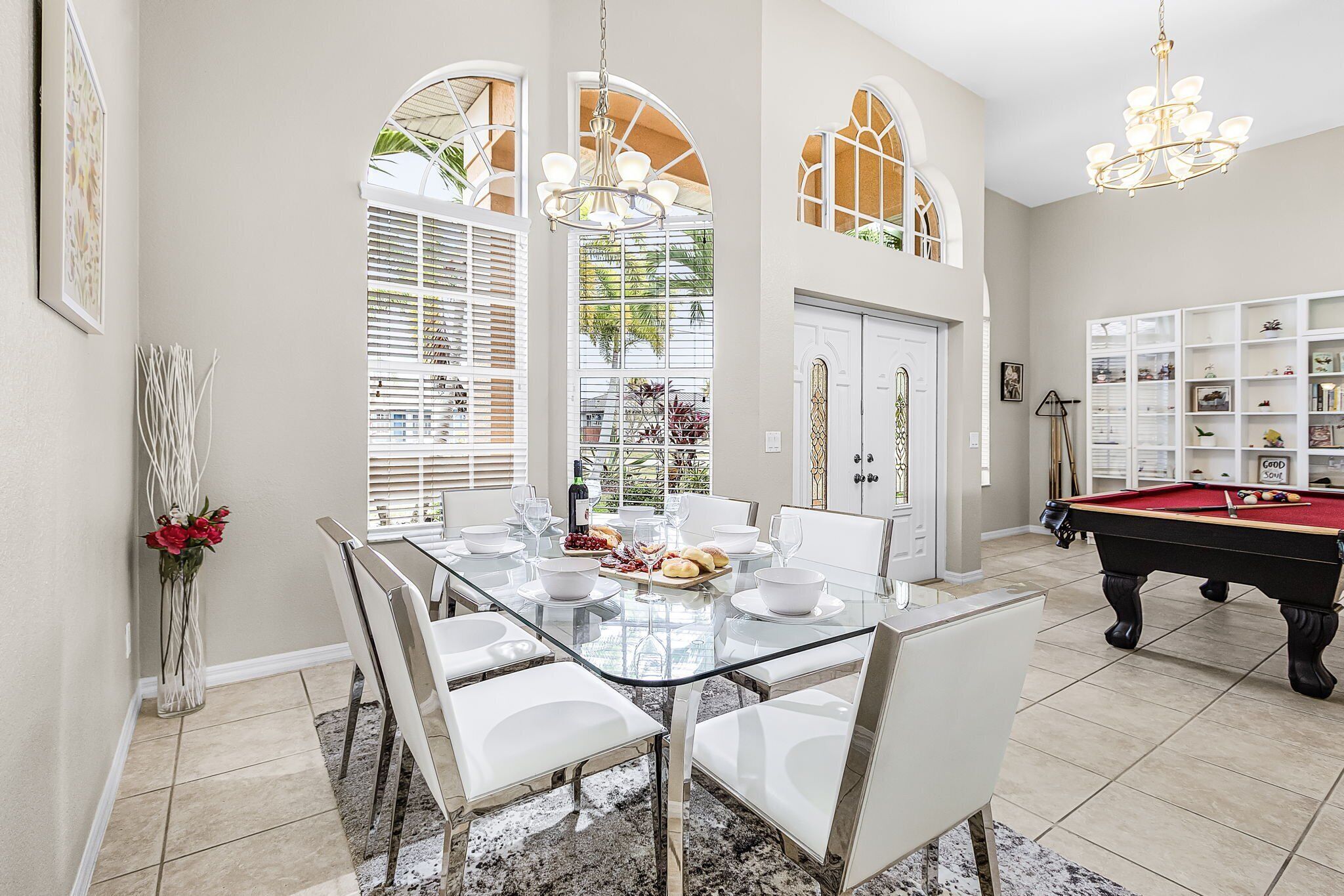 A dining area with a glass table, white chairs, and a pool table.