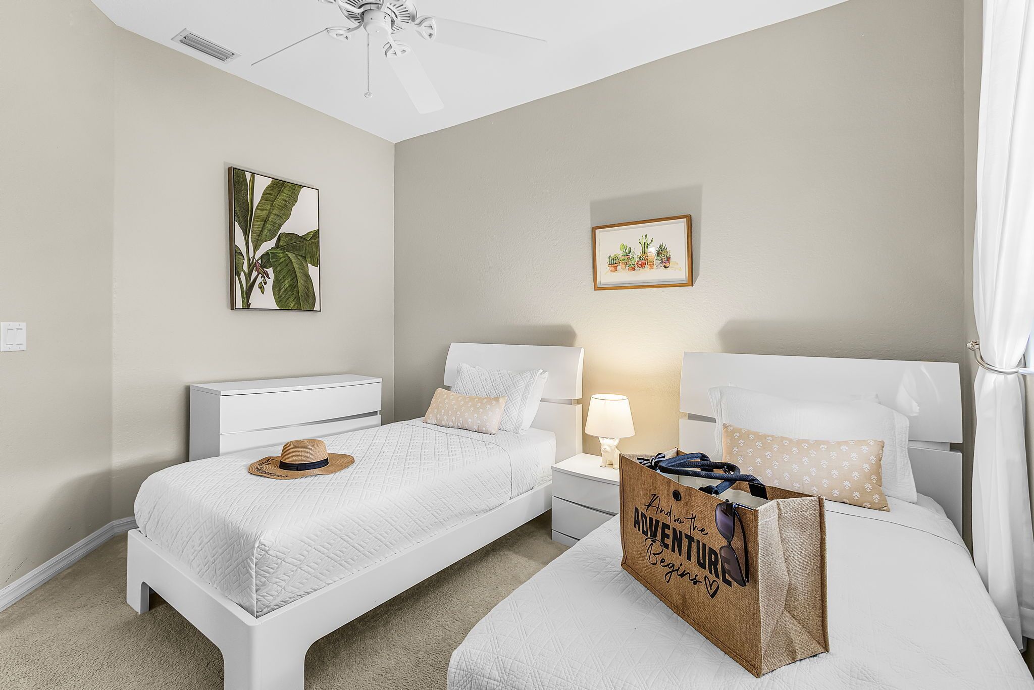 A bedroom with two beds, a ceiling fan, a nightstand with a lamp, and a bag labeled "And to the Adventure Begins".
