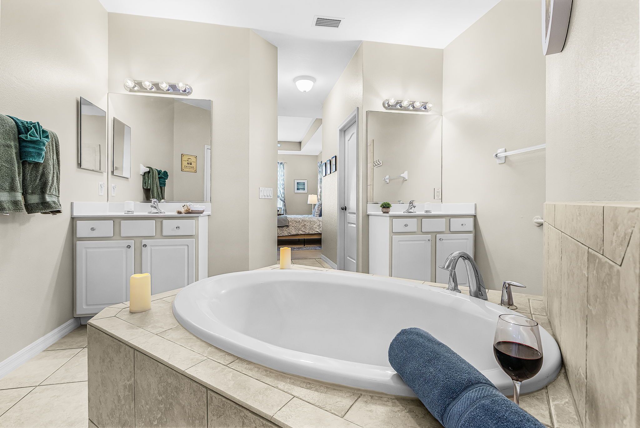A modern bathroom with a large bathtub, a vanity with a mirror, and a glass of red wine on the counter.