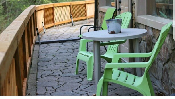 Une terrasse avec une table ronde et deux chaises vertes, une clôture en bois et un mur de pierre.
