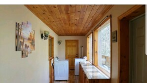 Un couloir étroit avec un plancher et des murs en bois, un lave-linge et une fenêtre donnant sur des arbres.