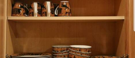 A wooden cabinet with shelves holding ceramic mugs and plates.