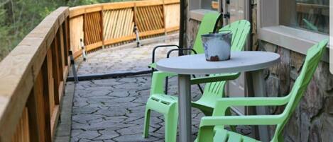 Un patio con una mesa redonda y dos sillas verdes, una cerca de madera y un muro de piedra.