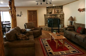Uma sala de estar acolhedora com lareira de pedra, sofás de couro e mesa de centro de madeira.