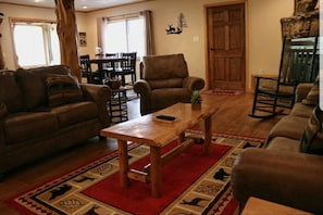 Uma sala de estar com uma mesa de centro de madeira, dois sofás, uma mesa de jantar com cadeiras e um tapete vermelho com estampas de animais.