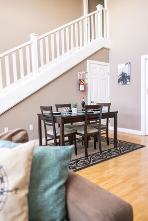 A dining area with a wooden table and chairs, a staircase, and a fire extinguisher on the wall. - Comfort and Convenience in Downtown Sitka - Suite A (Sitka)