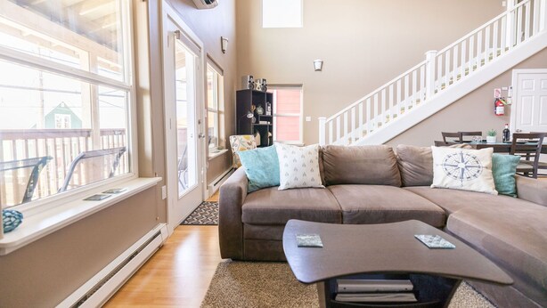 A living room with a brown sectional sofa, a coffee table, and a staircase. - Comfort and Convenience in Downtown Sitka - Suite A (Sitka)