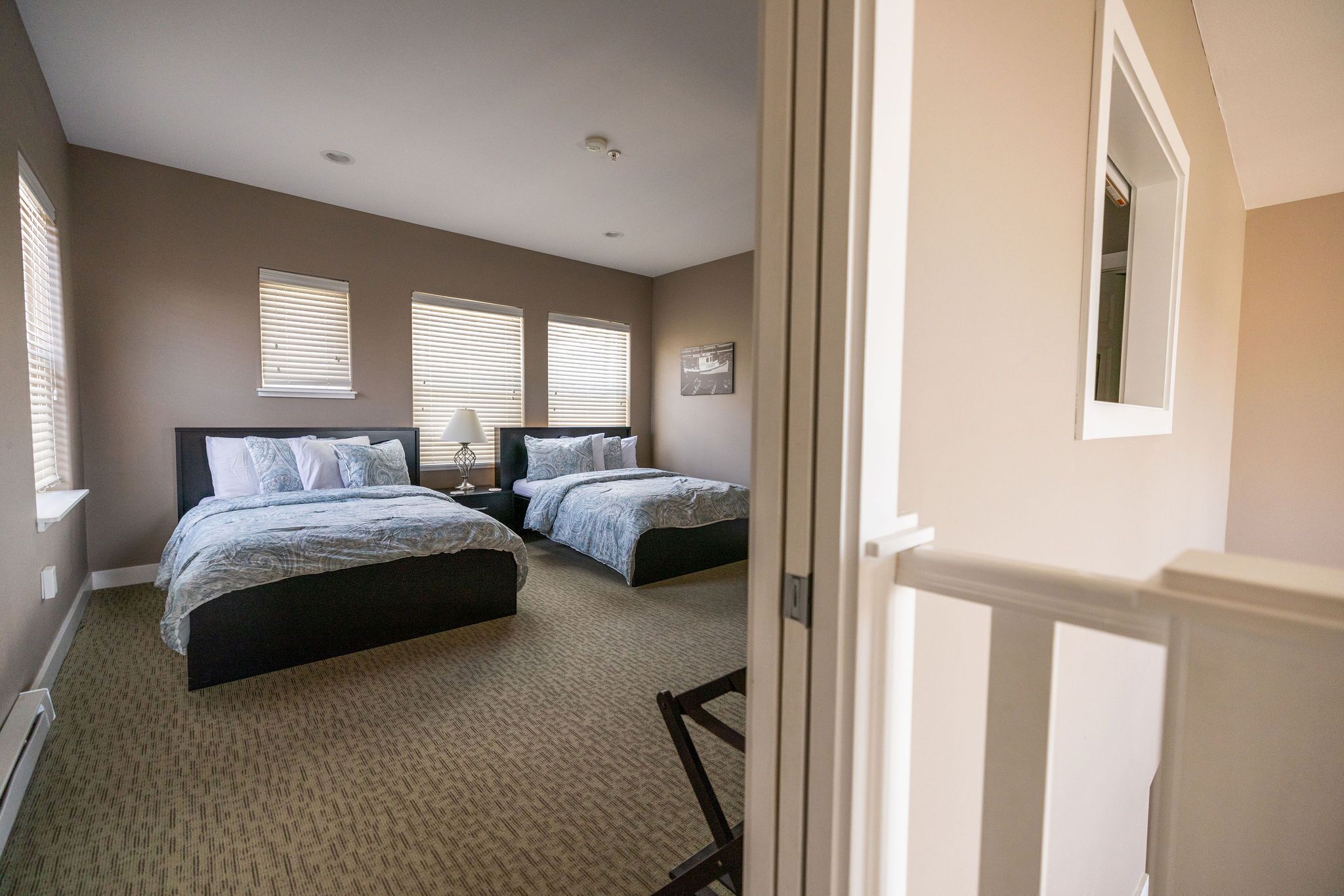 A bedroom with two beds, a nightstand, a lamp, and a window with blinds.
