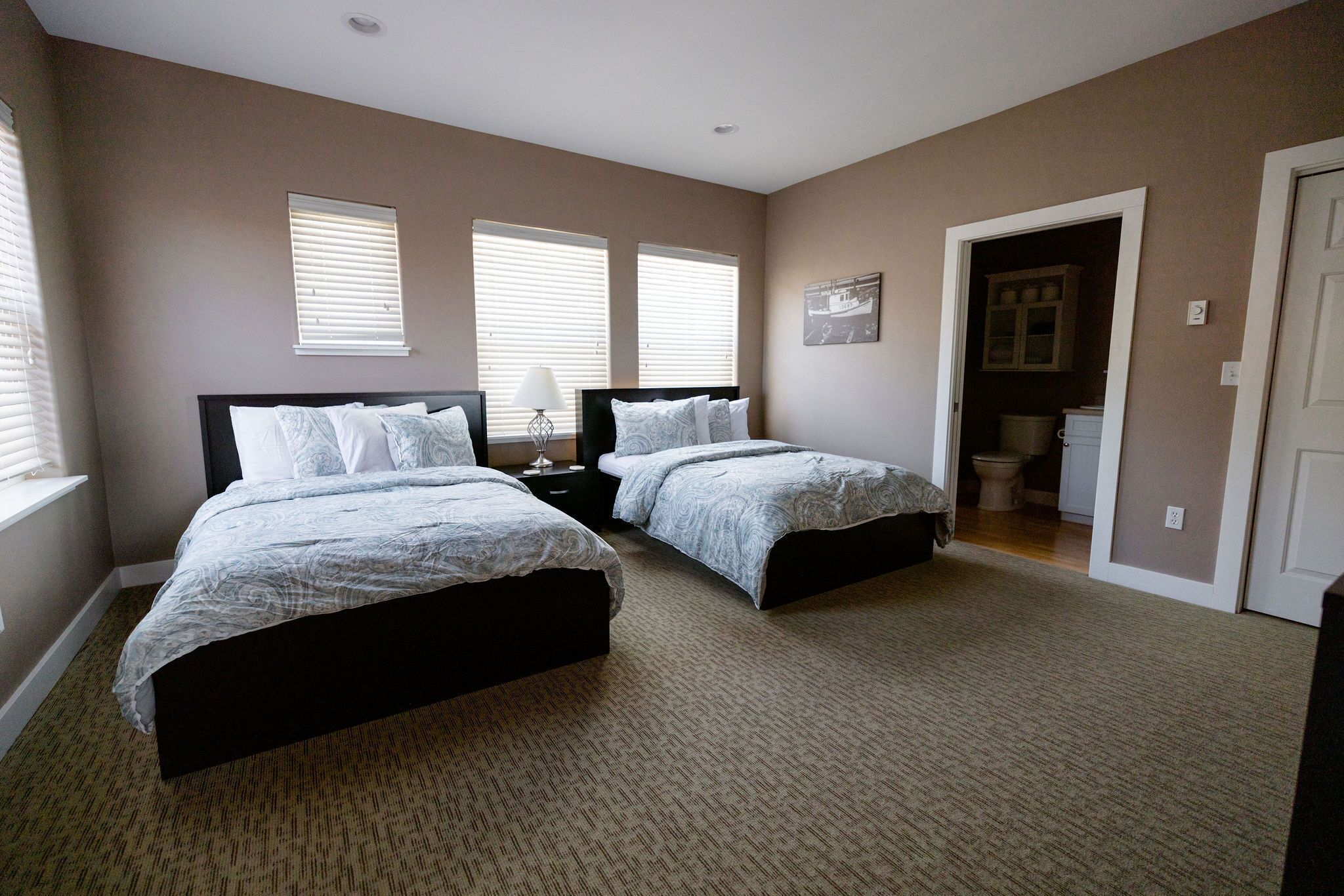 A bedroom with two beds, a carpeted floor, and a door leading to a bathroom.