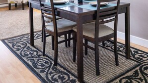 A dining area with a wooden table and chairs, a rug, and a staircase in the background. - Comfort and Convenience in Downtown Sitka - Suite A (Sitka)