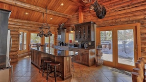 L’intérieur d’une cabane en rondins, avec un îlot central, des tabourets de bar, des meubles en bois et une tête de wapiti fixée au mur.