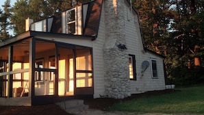 A modern house with a stone exterior, large windows, and a covered porch. - Charming Lake Cottage est 1903! Private and relaxing waterfront, family fun! (Rindge)