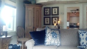 A living room with a sofa, a wooden cabinet, and framed artwork on the wall. - Charming Lake Cottage est 1903! Private and relaxing waterfront, family fun! (Rindge)